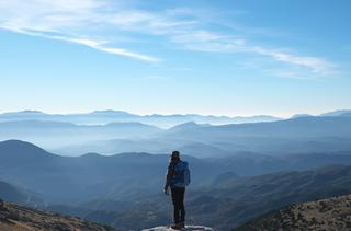 A person, standing on top of a hill, overlooking a vast landscape of hills.