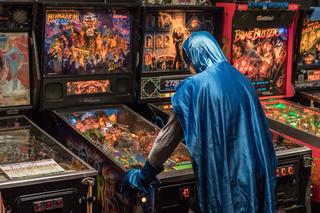 A man in a Batman costume, playing Pinball